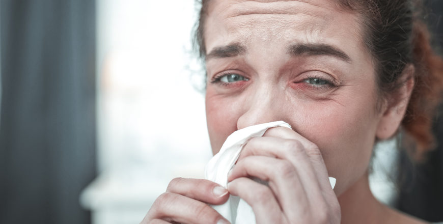 Green-eyed woman drying her running nose after strong allergy